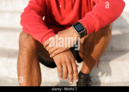 Nahaufnahme der afrikanischen Mann im T-Shirt sitzen im Freien, das Tragen von smart Watch Stockfoto