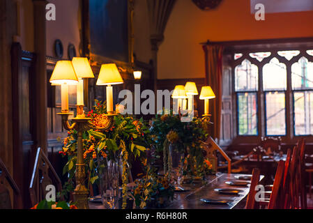 In der Nähe von mittelalterlichen britischen schloss Innenbereich Esstisch mit Platten, die Blumen und die Lampen. Warmes Licht. Selektiver Fokus. Kopieren Sie Platz Stockfoto