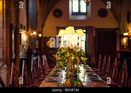 Mittelalterliche britischen schloss Innenbereich Esstisch mit Platten, die Blumen und die Lampen. Warmes Licht. Selektiver Fokus. Kopieren Sie Platz Stockfoto