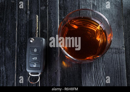 Autoschlüssel und Whiskey Alkohol in einem Glas auf schwarzen Holztisch. Trinken Sie nicht und abstraktes Konzept. Stockfoto