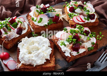 Smorrebrod - Dänische offen stehen Sandwiches mit geräucherter Makrele Schichten, Creme gemischt mit geriebenem Meerrettich, Rote Bete, frische Radieschen, Zwiebeln auf einem dunklen Stockfoto