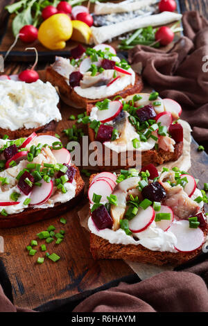 Smorrebrod - Dänische offen stehen Sandwiches mit geräucherter Makrele Schichten, Creme gemischt mit geriebenem Meerrettich, Rote Bete, frische Radieschen, Zwiebeln auf einem dunklen Stockfoto