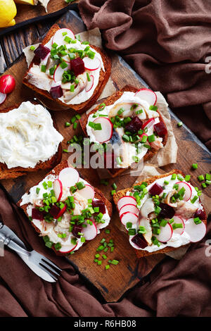 Smorrebrod - Dänische offen stehen Sandwiches mit geräucherter Makrele Schichten, Creme gemischt mit geriebenem Meerrettich, Rote Bete, frische Radieschen, Zwiebeln auf einem dunklen Stockfoto