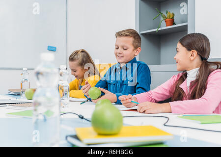 Glückliche Kinder sitzen am Schreibtisch im Klassenzimmer Stockfoto