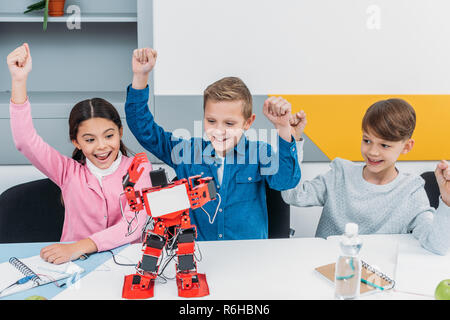 Glückliche Schüler heben die Hände und Suchen an der rot handgefertigte Roboter an der Rezeption während Stammzellen Lektion Stockfoto