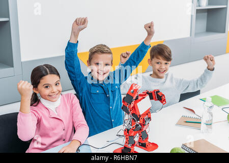 Kinder freue mich und heben die Hände am Schreibtisch mit elektrischen Roboter während Stammzellen Lektion Stockfoto