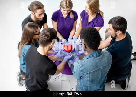 Gruppe von Menschen Holding mit Händen in medizinische Handschuhe rote Herzen Modell. Gesundes Herz Konzept Stockfoto