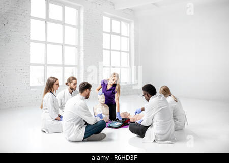 Gruppe junger Mediziner mit Ausbilder zeigt, wie Defibrillation auf das Dummy während der erste Hilfe Training zuhause tun Stockfoto