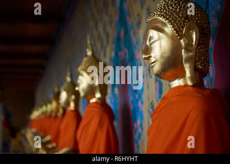 Mehrere Golden Buddha Statuen aufgereiht in einer abnehmenden Perspektive unter der Abdeckung eines der Ordination Halle in Bangkok, Thailand. Stockfoto