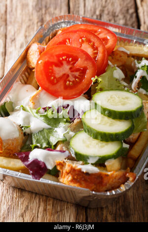 Kapsalon aus den Niederlanden: Pommes frites garniert mit shawarma Fleisch, dann Gouda Käse und frisches Gemüse Nahaufnahme auf dem Tisch. Vertikale Stockfoto