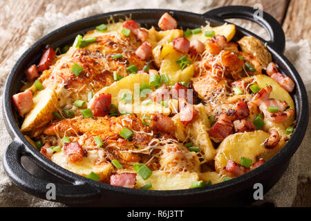 Leckere hausgemachte gebackene Hähnchenbrustfilet mit Kartoffeln, Speck und Käse close-up in einer Pfanne auf dem Tisch. Horizontale Stockfoto