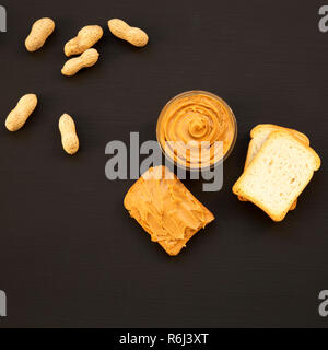 Schüssel mit Erdnussbutter, Toast, ohne schale Erdnüsse auf eine schwarze Fläche, Ansicht von oben. Von oben, Overhead, flach. Stockfoto