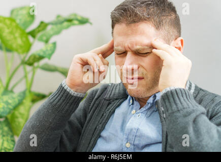 Stattliche unrasierte Mann mit Kopfschmerzen zu Hause. Stockfoto