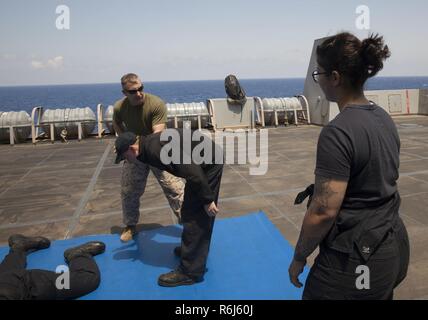 Gunnery Sgt. Arvin Manning, Personal noncommissioned Officer zuständig für die Strafverfolgung Loslösung, 24 Marine Expeditionary Unit (MEU), erklärt zum Elektriker Mate 3. Klasse Lujain Alshaikhkhaleel die Schritte zur Ausführung eines arm Manipulation Technik während es demonstrieren, während eine nicht tödliche Klasse als Teil des Master-at-arms Ausbildung an Bord amphibious Transport dock Schiff USS Mesa Verde LPD (19) 18. Mai 2017. Die 24. MEU ist mit dem Bataan Amphibious Ready Gruppe unterwegs in der Unterstützung der Maritime Security Operations und Theater Sicherheit Zusammenarbeit in den USA 6 Flotte Einsatzgebiet Stockfoto