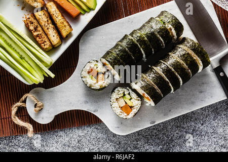 Vegan Ready-made Sushi auf dem Tisch in Fisch. Brötchen mit gebratenem Tofu, Gurken, gekochte Karotten und frischen Avocado. Gesunde vegane Ernährung Stockfoto
