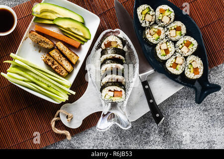 Vegan Ready-made Sushi auf dem Tisch in Fisch. Brötchen mit gebratenem Tofu, Gurken, gekochte Karotten und frischen Avocado. Gesunde vegane Ernährung Stockfoto