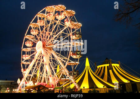 03. Dezember 2018, Hessen, Kassel: Das Riesenrad dreht sich auf dem märchenhaften Weihnachtsmarkt auf der blauen Stunde. Auf der rechten Seite die Zelte der Zirkus Flic Flac. Foto: Uwe Zucchi/dpa Stockfoto