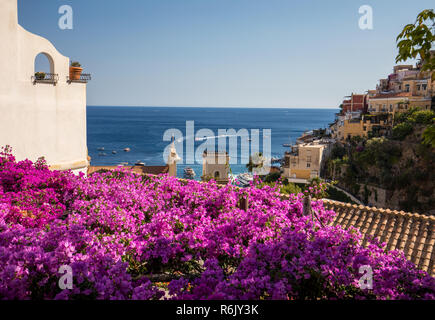 Positano durch rosafarbene Bougainvillea und Boote im Hintergrund eingerahmt. Bunte Positano, das Juwel der Amalfi Küste, mit seinen bunten Häusern und Gebäuden auf einem großen Hügel mit Blick auf das Meer. Italien Stockfoto