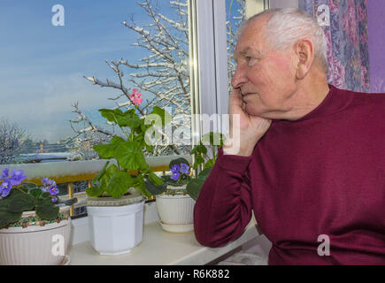 Alte einsame Mann sitzt in der Nähe der Fenster in seinem Haus. Stockfoto