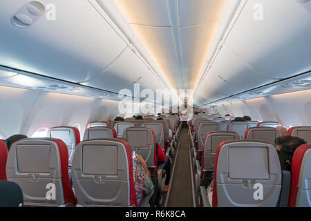 Innenraum des Flugzeug mit Passagieren auf Sitze und Stewardessen in Uniform zu Fuß den Gang. Stockfoto