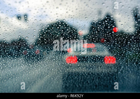 Regentropfen auf der Windschutzscheibe an einem regnerischen Tag; verschwommen Auto an einer Ampel im Hintergrund gestoppt; Kalifornien Stockfoto