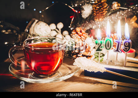 Neues Jahr Karte mit einer Tasse Tee in der Nähe von geschmückten Weihnachtsbaum und brennende Kerzen 2019. Frohes Neues Jahr Stockfoto