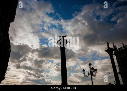 Venezianische geflügelte Löwe antike Statue an der Spitze der mittelalterlichen Spalte, errichtet im Jahre 1172, unter Wolken, in St. Markusplatz in Venedig Stockfoto