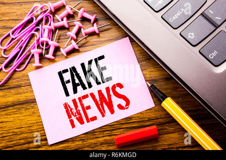 Handschriftlichen Text, gefälschte Nachrichten. Business Konzept für Hoax Journalismus auf rosa Zettel Papier auf dem hölzernen Hintergrund neben Tastatur geschrieben. Mit rotem Stift. Stockfoto