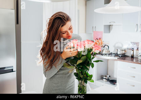 Junge Frau gefunden Blumenstrauß aus Rosen geschmückt mit Karte auf Küche. Gerne begeistert Mädchen duftende Blumen Stockfoto