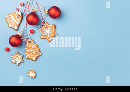 Gingerbread cookies mit roten Weihnachtskugeln hängt über blauen Hintergrund und mit Beeren dekoriert. Ansicht von oben, kopieren. Stockfoto