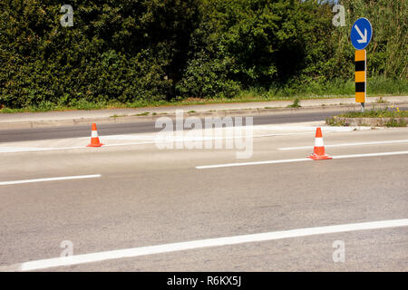 Die Arbeit auf der Straße. Bau Kegel mit Verkehrsschild rechts Zeichen halten. Leitkegel, mit weißen und orangefarbenen Streifen auf dem Asphalt. Verkehrszeichen. Stockfoto