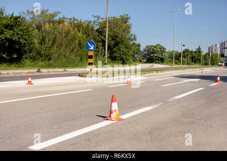 Die Arbeit auf der Straße. Bau Kegel mit Verkehrsschild rechts Zeichen halten. Leitkegel, mit weißen und orangefarbenen Streifen auf dem Asphalt. Verkehrszeichen. Stockfoto
