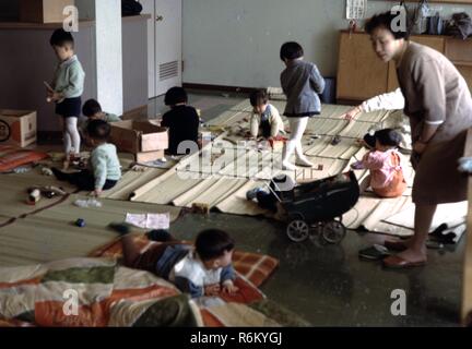 Eine Frau Uhren mehrere Kinder, die auf den traditionellen Bambus Matts spielen, in eine Vorschule Unterricht an einer christlichen missionarischen Kirche in der Nachkriegszeit in Japan, 1961. () Stockfoto