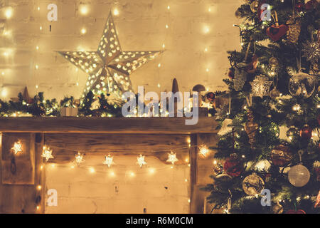 Das schön eingerichtete Holz Kaminsims, beleuchtete Weihnachtsbaum mit Kugeln und Ornamente, Holzdekorationen, Silver Star, Eiszapfen leuchten, getönt Stockfoto