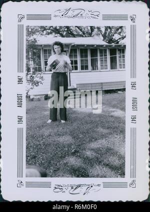 Frau, die auf dem Rasen eines Vorstadthaus und halten eine Kodak Brownie box Kamera, eine Ikone des frühen 20. Jahrhunderts Kamera, dekoriert mit einem reich verzierten Rahmen, August, 1947 gedruckt. () Stockfoto