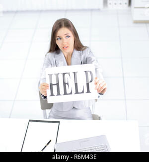 Business Frau mit einem Schild, auf dem Helfen, sitzen hinter einem Schreibtisch Stockfoto