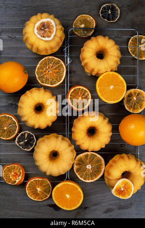 Kleine orange bundt Kuchen mit frischen und trockenen Orangen auf Kühlung ruck, Ansicht von oben, flach, vertikale Zusammensetzung Stockfoto