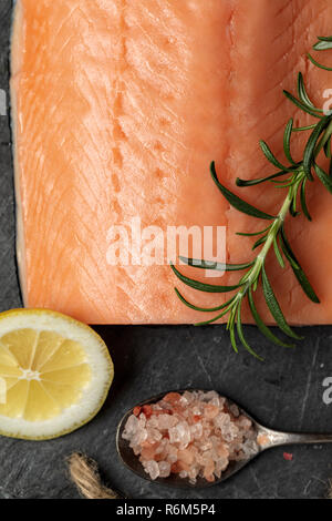 Roher Lachs filet auf schwarzem Schiefer Platte und Zutaten für die Herstellung von Graved Lachs. Salz, Zucker, Zitrone und Rosmarin im Hintergrund für trockene Heilung Marinade, da Stockfoto