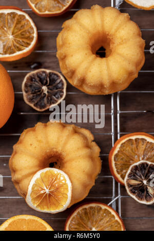 Kleine orange bundt Kuchen mit frischen und trockenen Orangen auf Kühlung ruck, Ansicht von oben, flach, Nahaufnahme, vertikale Zusammensetzung Stockfoto
