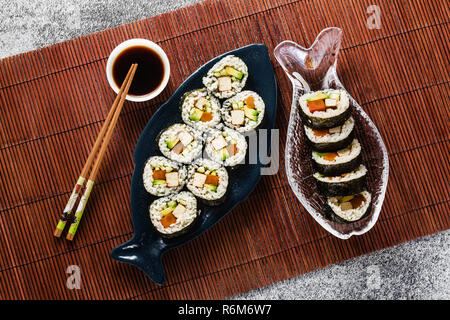 Vegan Ready-made Sushi auf dem Tisch in Fisch. Brötchen mit gebratenem Tofu, Gurken, gekochte Karotten und frischen Avocado. Gesunde vegane Ernährung Stockfoto