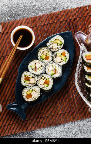Vegan Ready-made Sushi auf dem Tisch in Fisch. Brötchen mit gebratenem Tofu, Gurken, gekochte Karotten und frischen Avocado. Gesunde vegane Ernährung Stockfoto