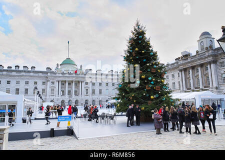 Weihnachtszeit in Somerset House in London. Weihnachtsbaum und Gruppe von Teenagern. Eislaufen hinter dem Baum. Stockfoto