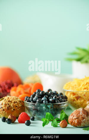 Köstliches Frühstück Zutaten. Corn Flakes, Nüsse, Früchte, Beeren, Milch, Joghurt, Orange, Banane, Pfirsich auf blauem Hintergrund. Kopieren Sie Platz. Stockfoto