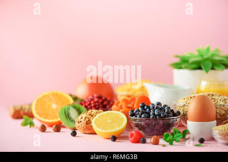 Frühstück serviert mit weich gekochte Eier, Haferflocken, Nüsse, Früchte, Beeren, Milch, Joghurt, Orange, Banane, Pfirsich auf rosa Hintergrund. Gesunde Ernährung Stockfoto