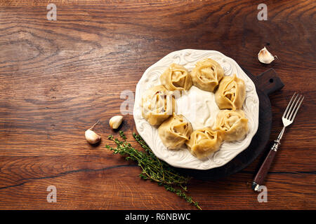 Asiatische gedünstete Teigtaschen Manti mit Dill und Knoblauch auf Holz- Hintergrund. Kopieren Sie Raum für Design. Stockfoto