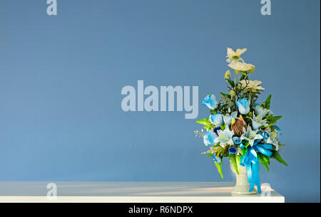 Blumenstrauß künstliche Blumen Vase auf Elfenbein Tabelle mit blauen Wand Stockfoto