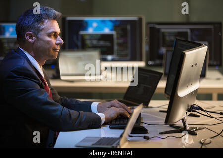 Geschäftsmanns, der auf mehreren Computern Stockfoto