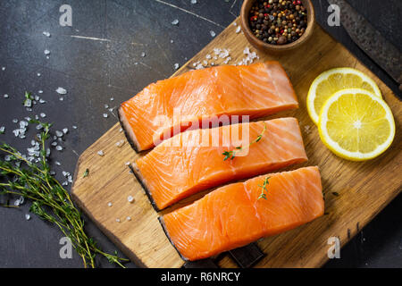 Frischen Fisch. Rohes Lachsfilet, Zitrone und Gewürze auf einem rustikalen Holzbrett auf einem Tisch aus Stein. Kopieren Sie Platz. Stockfoto