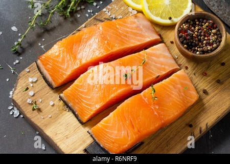 Frischen Fisch. Rohes Lachsfilet, Zitrone und Gewürze auf einem rustikalen Holzbrett auf einem Tisch aus Stein. Stockfoto
