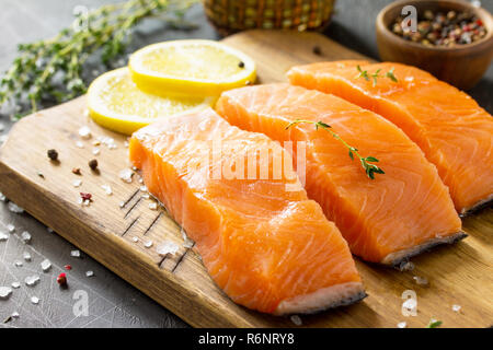 Frischen Fisch. Rohes Lachsfilet, Zitrone und Gewürze auf einem rustikalen Holzbrett auf einem Tisch aus Stein. Stockfoto